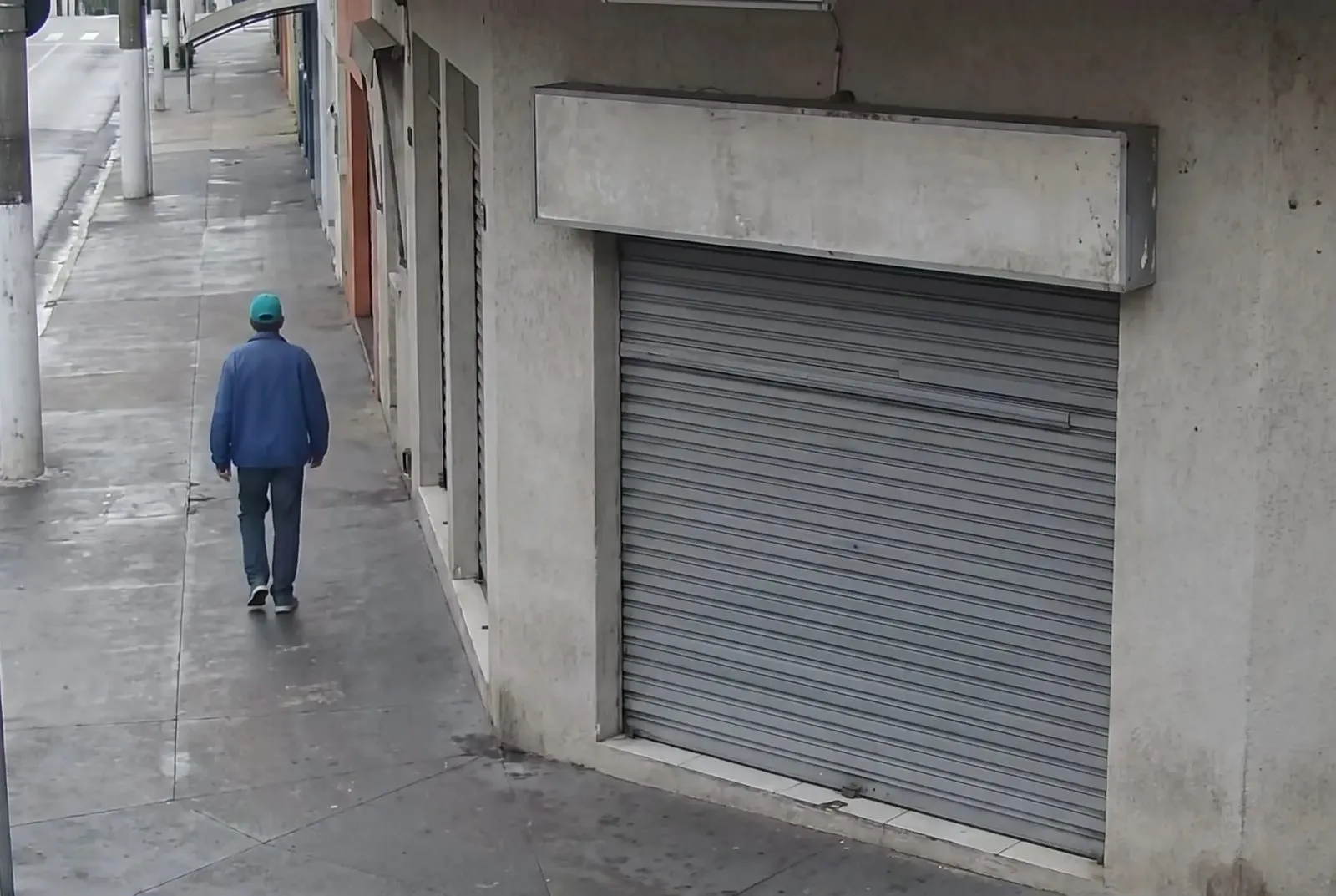Fachada da loja com a porta de enrolar fechada e um pedestre na calçada
